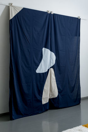 Photo of an art work made of dark blue fabric with two ambiguous, light coloured forms in the middle