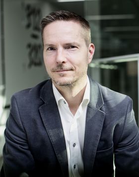 Adjunct Professor Matti Kuittinen in a white shirt and blue blazer staring directly into the camera.