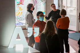 People chatting with each other in Space 21 housewarmng event. Aalto A-logo on the table in the front left of the picture.
