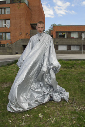 Nuori mies seisoo ulkona harmaasta pressusta tehty väljä mekkomainen vaate yllään