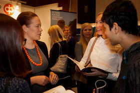 Four people are standing close to eachother in a crowd and talking. One of them is holding a book and they are smiling.