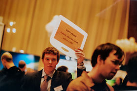 A man waring a suit is walking in a crowd and holding above his head a piece of paper with Finnish texts.