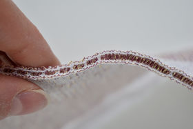 Fingers holding a piece of cloth that has some electronics woven in the structure