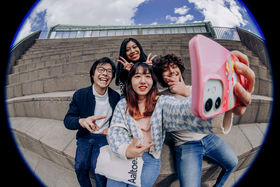 4 students taking a selfie on the steps of the Amphitheatre on Otaniemi Campus