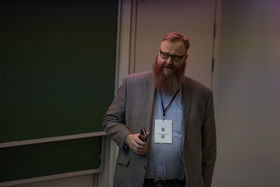 A man with a beard holding a mobile phone is looking away from the camera