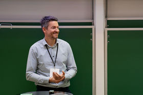 A man in a shirt smiling and looking away from the camera