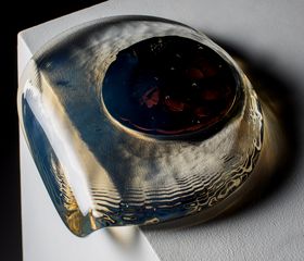 A transparent glass blob with a red blob inside it, pouring over the edge