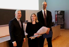 Palkittu hymyilemässä dekaanin ja varadekaanin kanssa