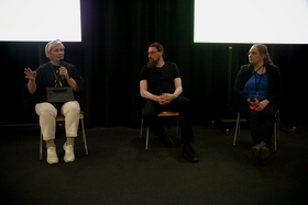 Three people sitting in a row with one holding a mic and talking.