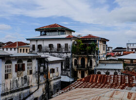 Historic buildings with weathered façades and red roofs in Zanzibar under a partly cloudy sky.