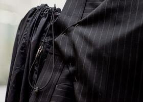 Close-up of a black pinstriped suit jacket with pins and black drawstring details.