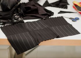 Black textured and striped fabric pieces on a white table, surrounded by sewing supplies including scissors.