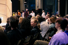 A group of people sitting on chairs and watching a performance or presentation indoors.