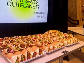 A table with many filled tortilla wraps in front of a screen displaying 'What saves our planet? A discussion 25.3.2025'.
