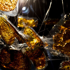 Close-up of shiny, golden foil tangled in thin threads, illuminated by a light source in a dark setting.