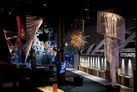 Modern art exhibition with abstract sculptures, including a red and white structure, golden tangled wires, and translucent spiral ribbons.