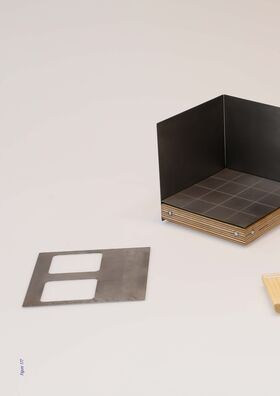 A metal structure with a wooden base next to a metal plate with two rectangular cutouts, and part of a wooden piece. The picture is from a diploma work by Nhung Pham.