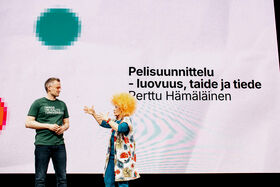 Two people in front of a presentation slide that reads 'Game Design - Creativity, Art and Science' by Perttu Hämäläinen.