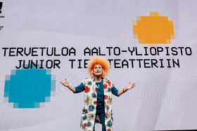Person with orange hair stands in front of text welcoming to Aalto University Junior Science Theatre.
