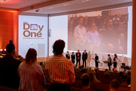 An event presentation in an auditorium with people standing on stage and audience members seated.