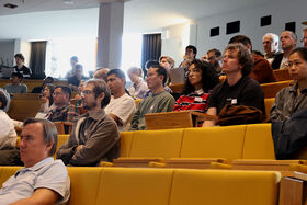 People seated in an auditorium with yellow seats, attentively listening to a presentation.