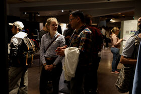Several people interacting in a crowded indoor event. One person holds a white jacket.