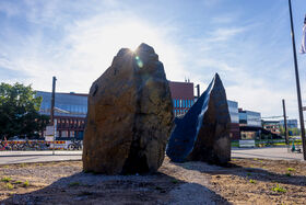 Två stora stenar framför universitetsbyggnader med solen som lyser bakom dem.