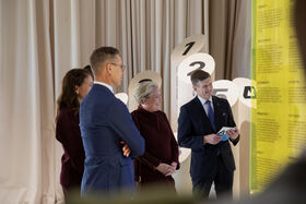 Group of people in formal attire examining an exhibit with numbered displays and informational panels.
