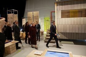 People are touring an exhibition featuring wooden structures and information panels about sustainable buildings.