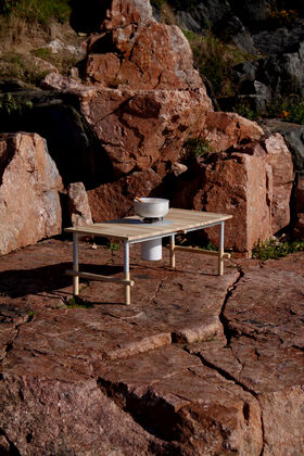 A small wooden table with a camping stove and pot on rocky terrain with large boulders in the background.