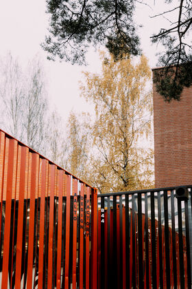 Vertical red and black beams with 'Aalto Design Factory' text. Autumn trees and brick building in the background.