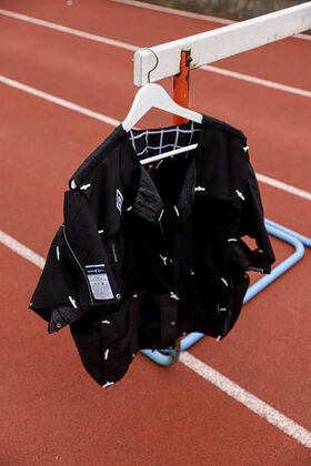 A black jacket with white details hangs on a white hanger on a red running track.