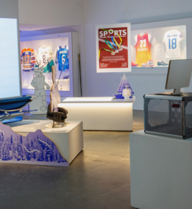 Exhibit with sports objects including jerseys, medals, and equipment in a modern museum setting.