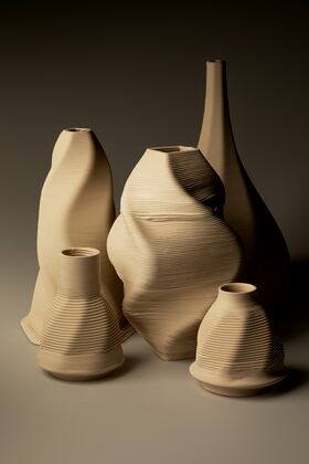 Five 3D-printed beige ceramic vases of varying shapes and sizes with textured surfaces, arranged on a neutral background.