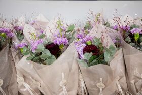 Kukkakimppuja, jotka on kääritty beigeen paperiin, sisältäen violetteja ja tummanpunaisia kukkia vihreillä lehdillä.