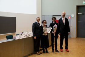 Neljä ihmistä seisoo sisällä, kolme pitää kimppuja. Vasemmalla pöytä, jossa lisää kimppuja. He ovat pukeutuneet muodollisesti.