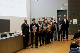 Ryhmä ihmisiä seisoo huoneessa pitäen kukkakimppuja. Taustalla näkyy esitysnäyttö ja tuoleja.