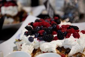 Jälkiruoka, jonka päällä on kermavaahtoa ja erilaisia marjoja, kuten vadelmia, mustikoita ja karhunvatukoita.