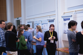 People are gathered around posters on a wall in a room, discussing and examining the information displayed.