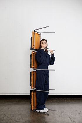 Person in blue overalls standing behind a stack of orange chairs held by metal bars.