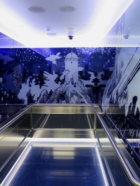 An elevator with a mural of a lighthouse on a rocky hill surrounded by trees and stars on the walls.