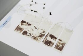 Five rectangular tags with abstract brown prints, connected by strings with black beads, displayed on a white surface.