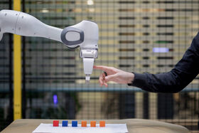 En robotarm och en människohand är på väg att röra vid varandra ovanför ett bord med färgglada block.