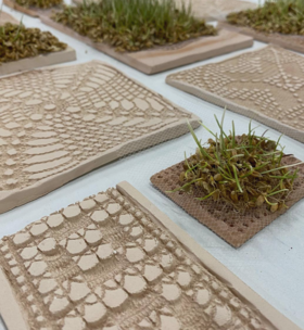 Clay tiles with intricate patterns and small patches of grass on a white surface.