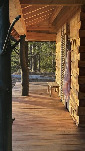 Wooden sauna porch with a bench and tree trunks as pillars. Forest in the background.