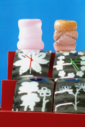 Two decorative objects on a red stand with flower designs and clock hands, set against a blue background.