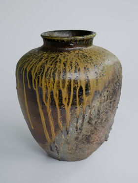 A rustic ceramic vase with a wide body and narrow neck, featuring yellow drips and textured surface.