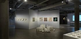 An art gallery with various sculptures and paintings. Conical sculptures are arranged on the floor.