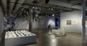 A modern art gallery with sculptures, wall art, and installations. The space has concrete floors and exposed pipes.