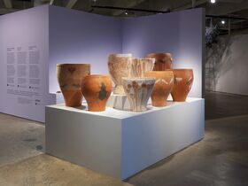 A display of large ceramic pots with various designs on a white pedestal in an art gallery with purple walls.